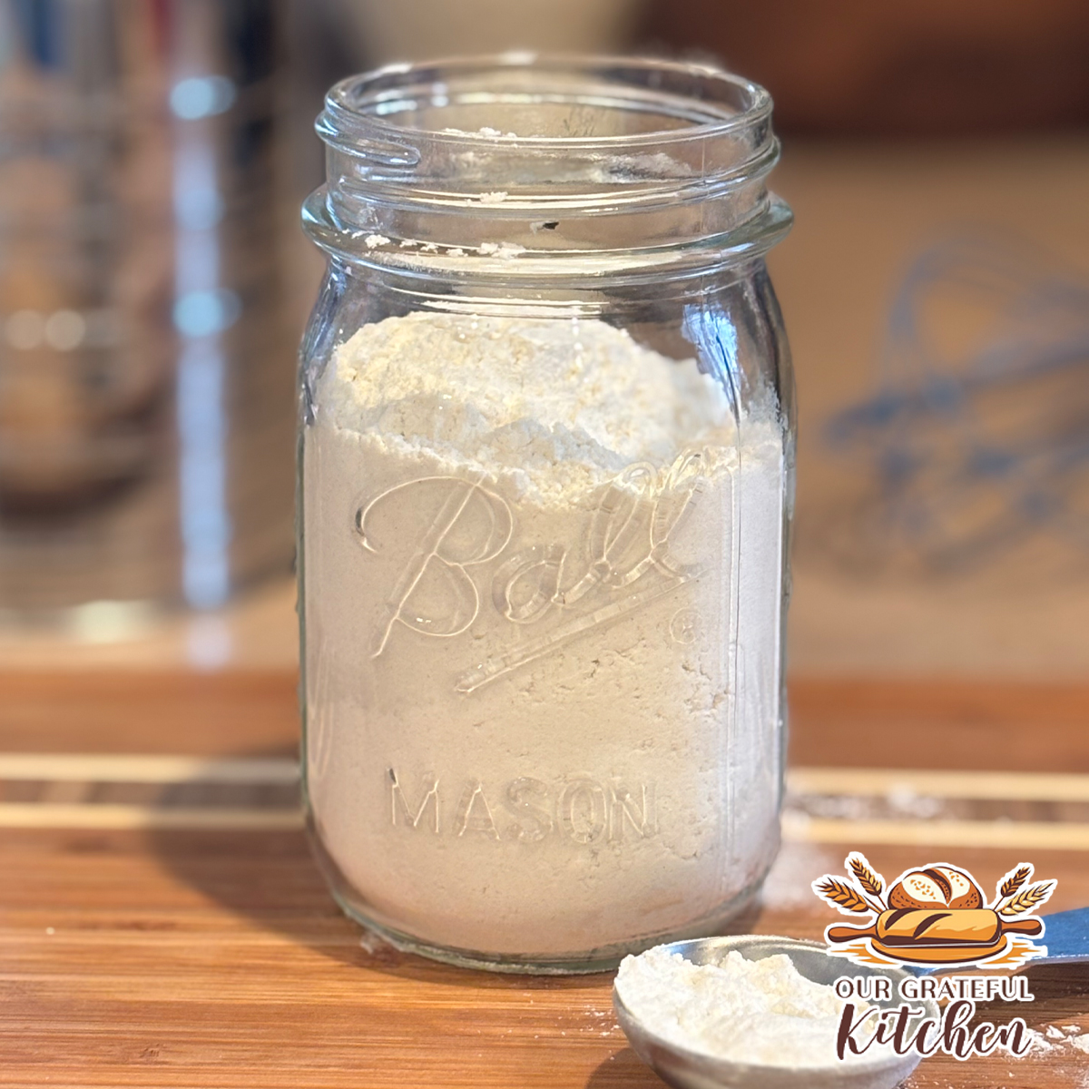 Homemade cake flour in a mason jar on a wooden board with a measuring scoop, flour sifter, and whisk in the background.