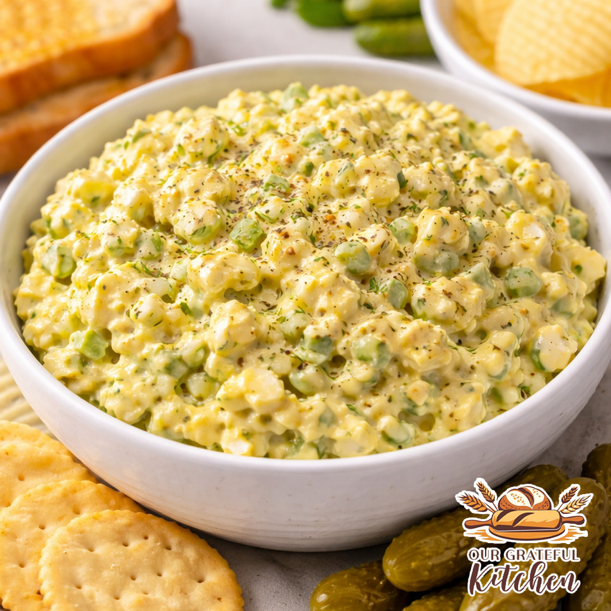 Creamy classic egg salad with Dijon mustard freeze dried chives and dill weed served in a bowl with crackers and mini dill pickles