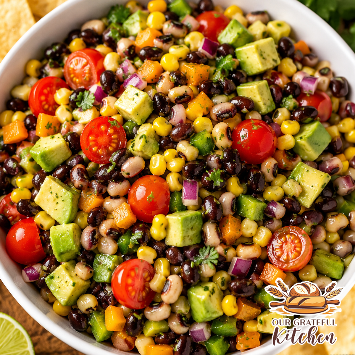 The Best Cowboy Caviar recipe served in a white bowl with black beans, black-eyed peas, corn, avocado, cherry tomatoes, bell peppers, cilantro, and tortilla chips for dipping.