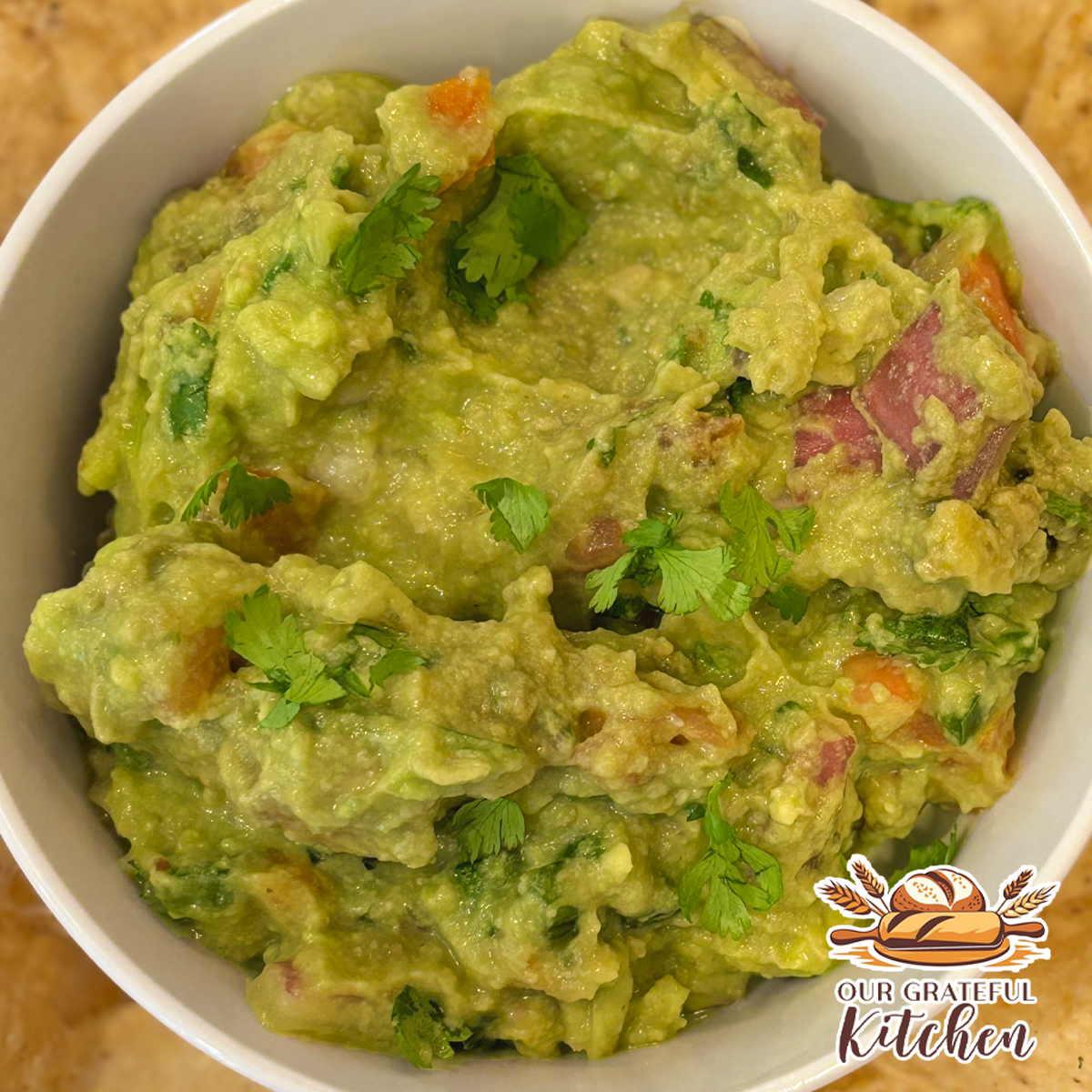 Easy homemade guacamole served in a white bowl with tortilla chips, featuring chunky avocado, tomatoes, red onion, cilantro, and jalapeño.