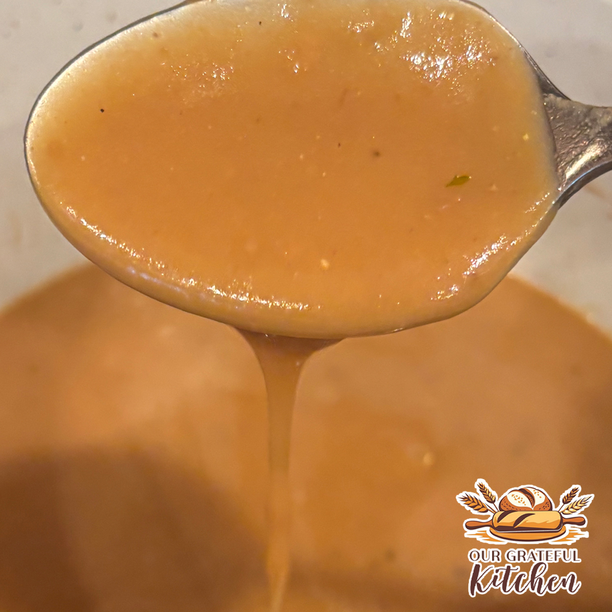 Homemade brown gravy dripping from a spoon into a saucepan, showing its rich, smooth texture.