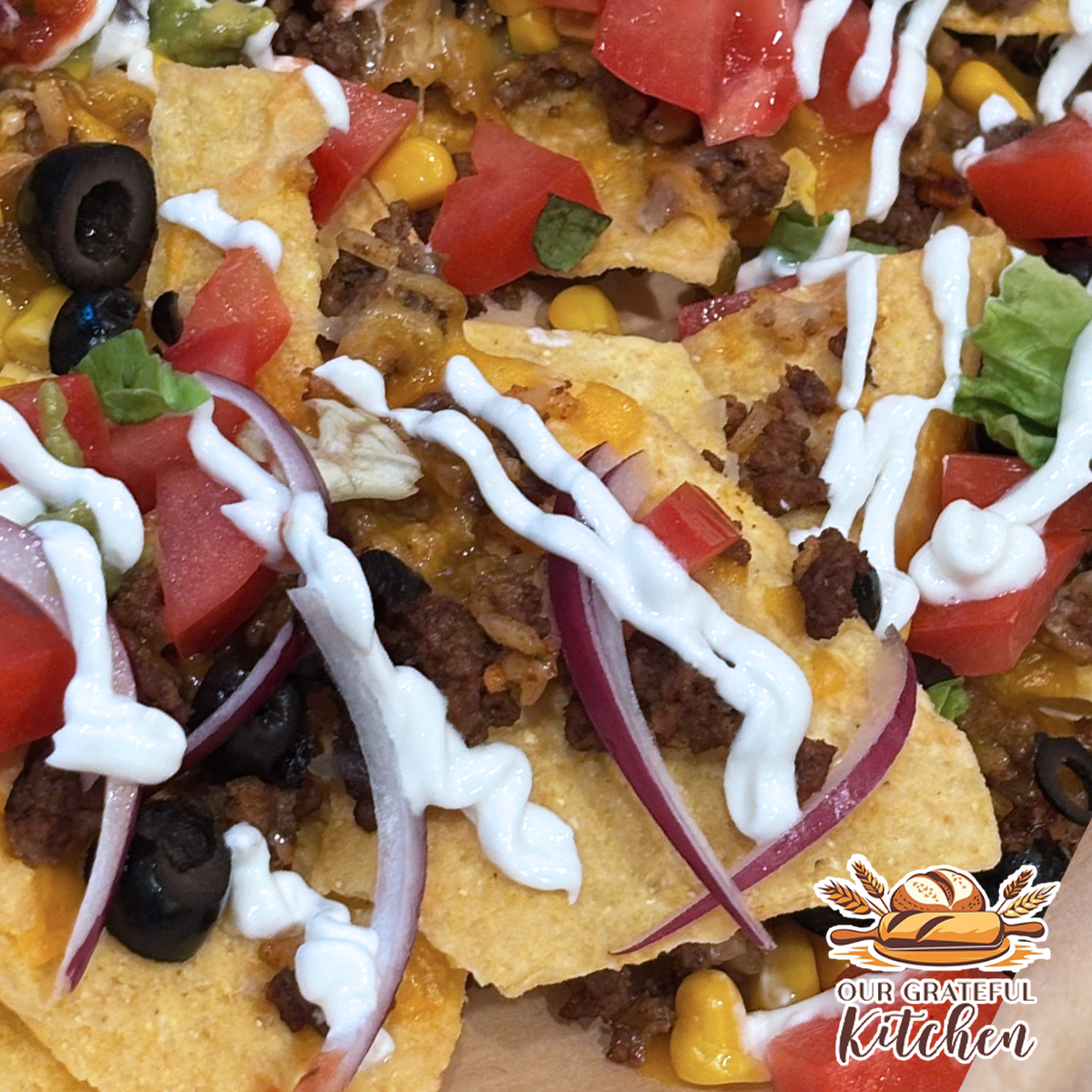 Loaded sheet pan nachos with ground beef, cheese, corn, tomatoes, black olives, red onion, and sour cream